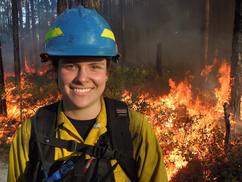 female firefighter smiling closeup, wildfire in background